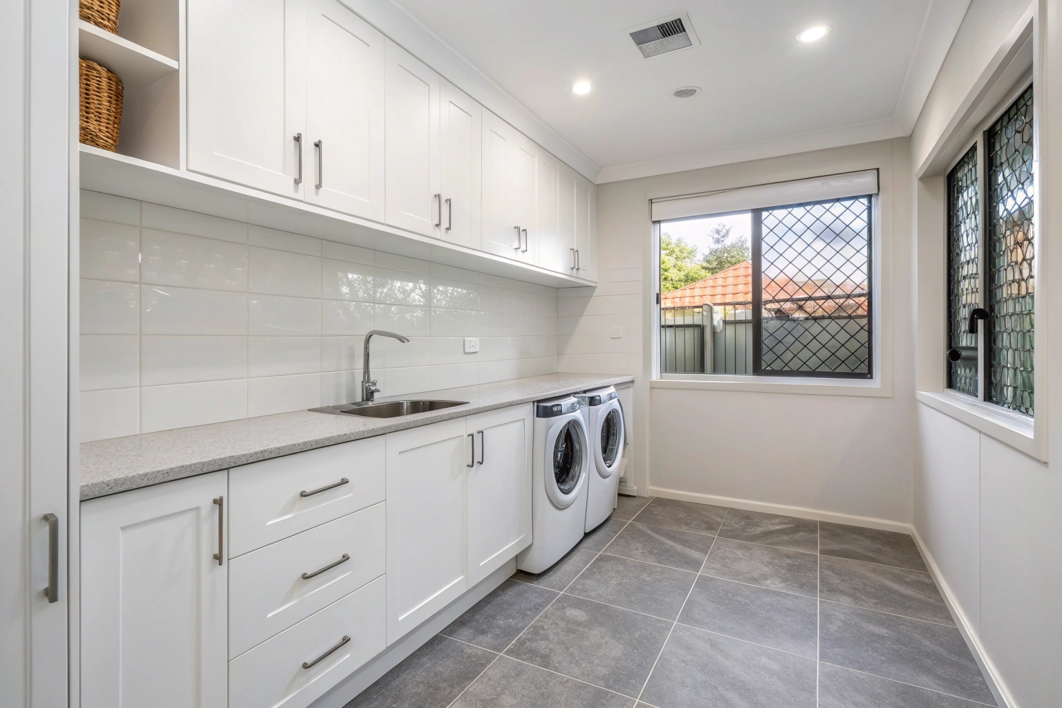 Renovated laundry room in Newcastle home with white cabinetry, stone benchtop and large format porcelain floor tiles